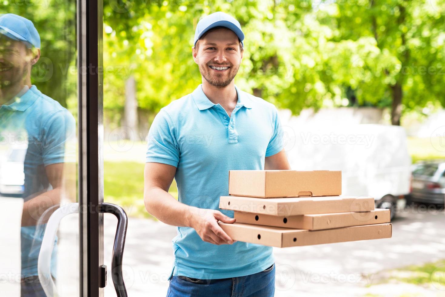 lächelnder Kurier während der Pizzalieferung in der Nähe eines Eingangs foto