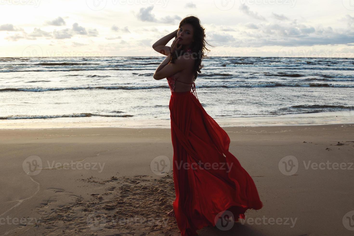 atemberaubende Frau, die ein wunderschönes rotes Kleid am Strand trägt foto