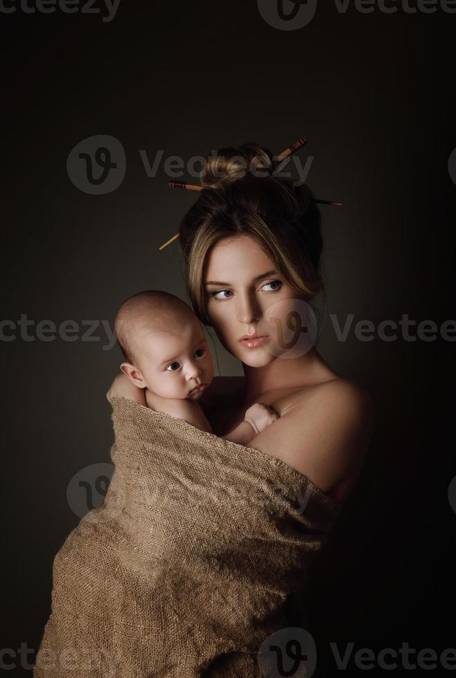 Schöne Mutter und ihr kleines Baby sind in Sackleinen gehüllt foto