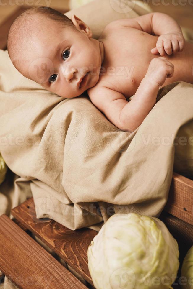 Das kleine Baby liegt in der Kiste mit vielen Kohlköpfen herum foto