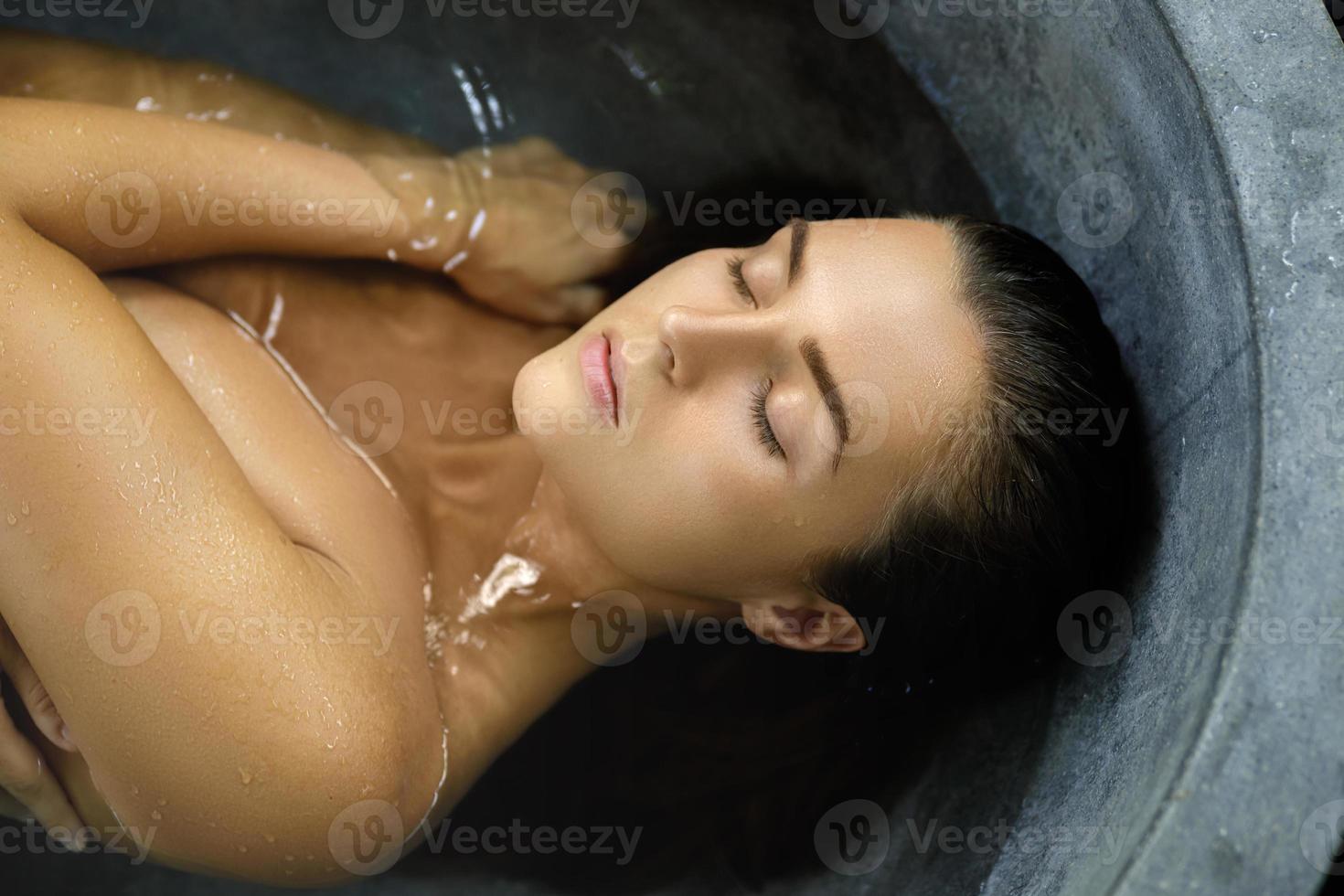 schöne frau, die in der steinbadewanne liegt und sich entspannt foto