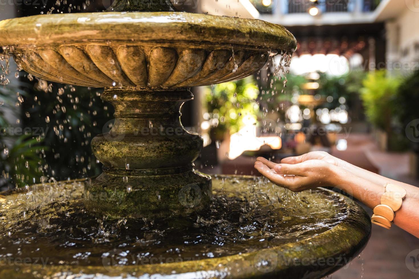 weibliche Hände alter Brunnen mit spritzenden Wassertropfen foto