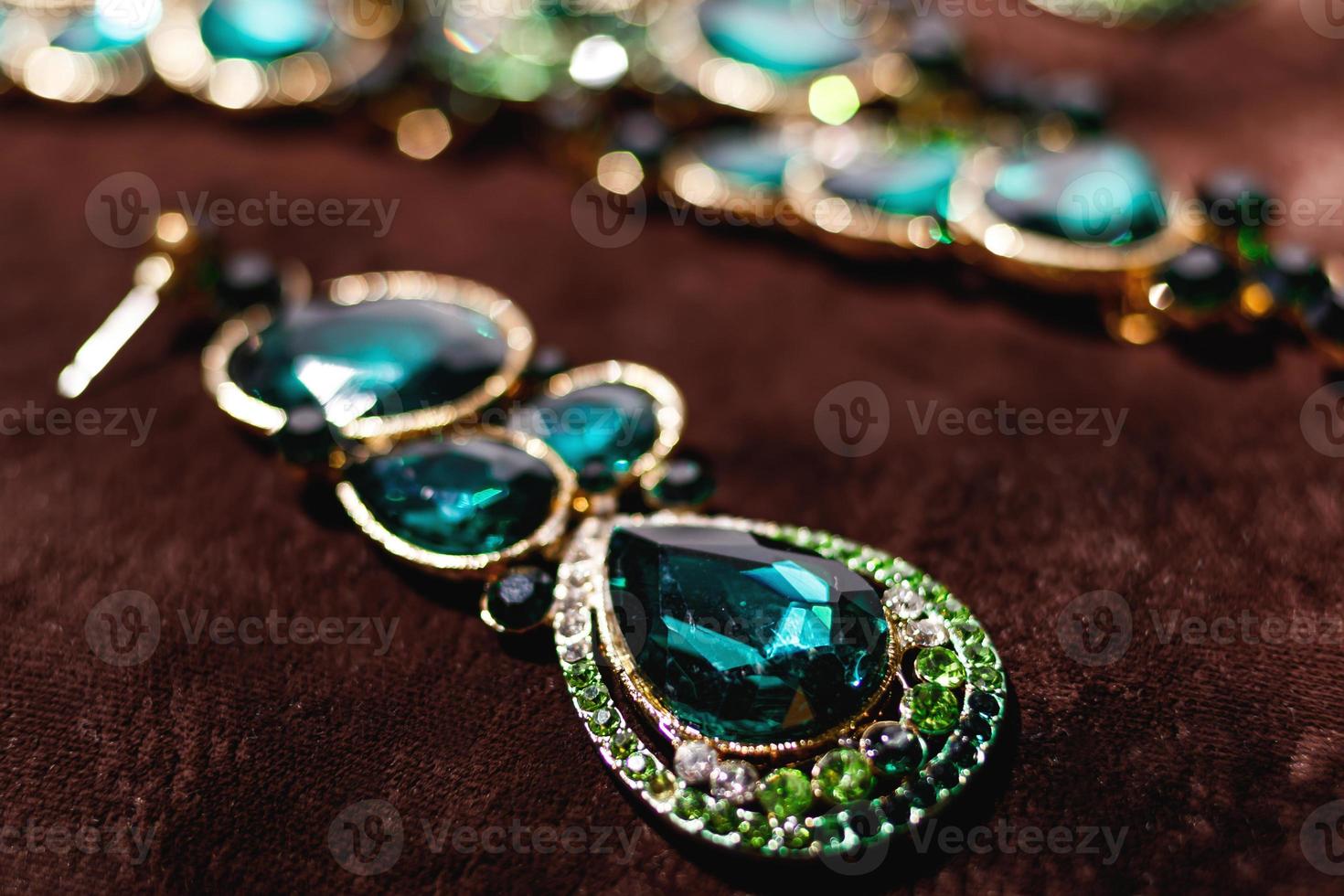 Luxusohrringe mit grünen Edelsteinen auf braunem Samt foto