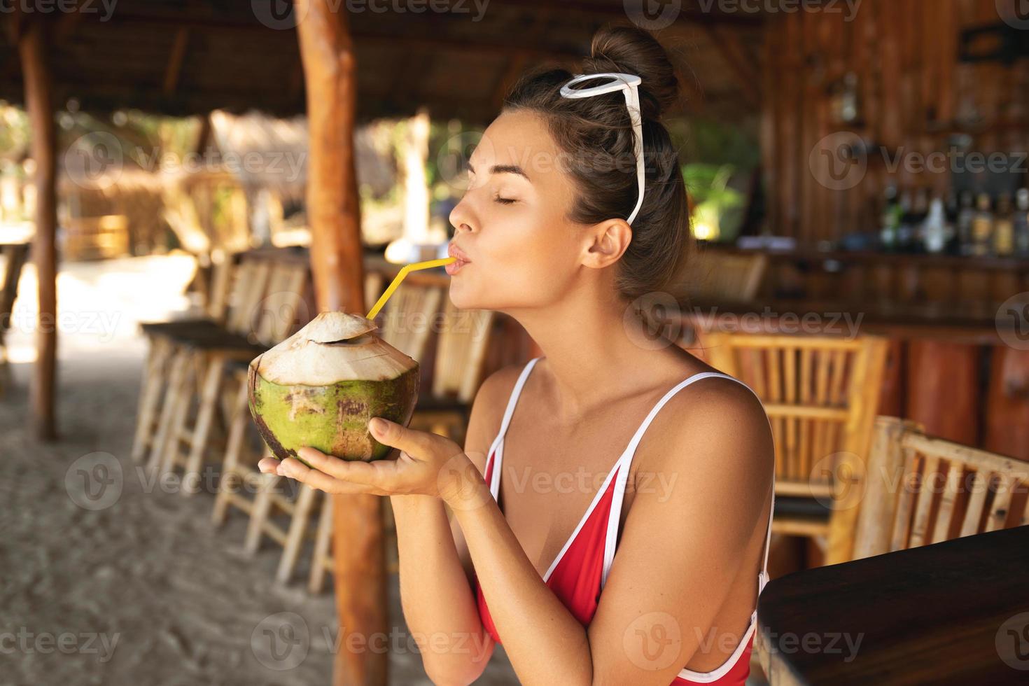 Junge und sexy Frau, die in einer authentischen Strandbar mit einem Kokosnussgetränk sitzt foto