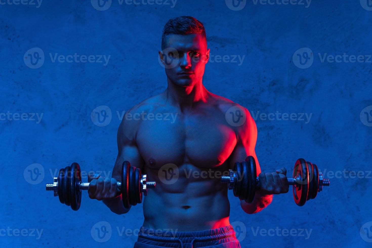 muskulöser bodybuilder, der mit hanteln in buntem neonlicht trainiert foto