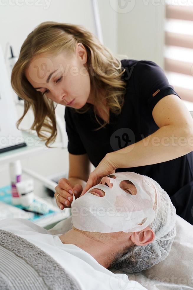 Kosmetikerin, die Blattmaske auf das Gesicht des Kunden aufträgt foto