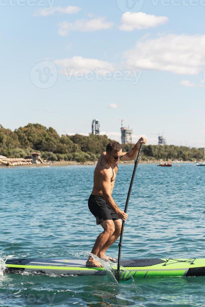 junger männlicher surfer, der standup-paddleboard im ozean reitet. foto