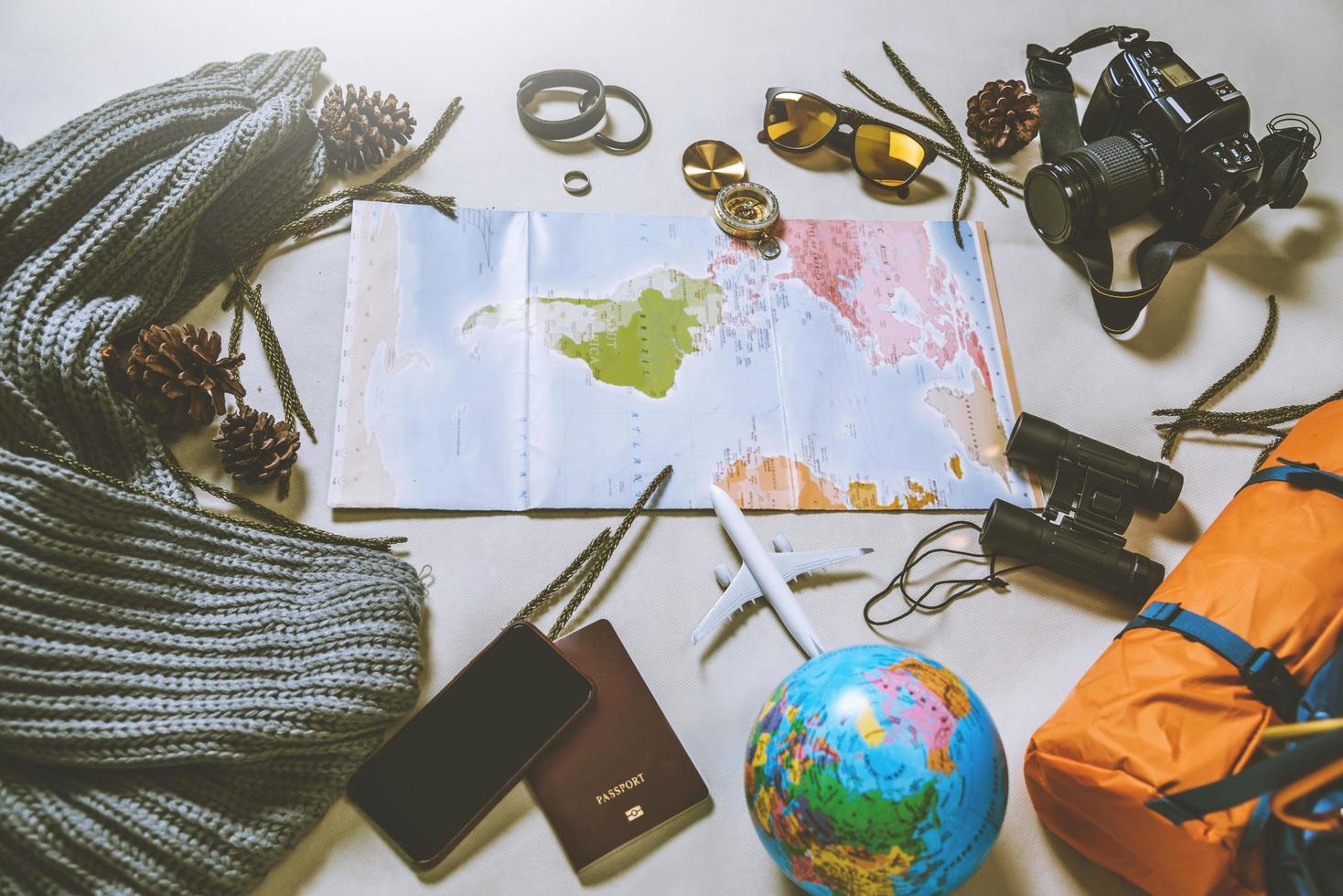 touristische Planung des Urlaubs mit Hilfe der Weltkarte mit anderem Reisezubehör. Smartphone, Filmkamera und Sonnenbrille auf weißem Hintergrund. Reiserucksack foto