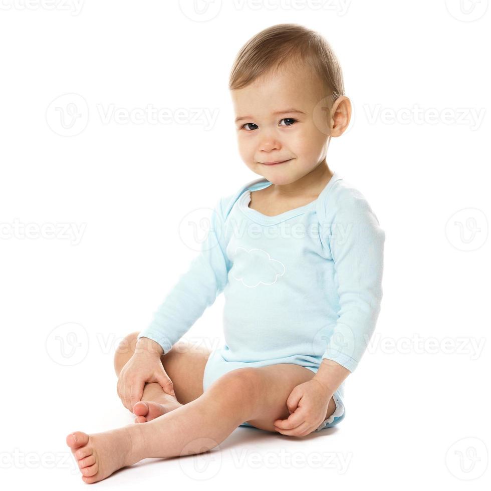 Neugieriger kleiner Junge im Strampler sitzend und lächelnd. foto