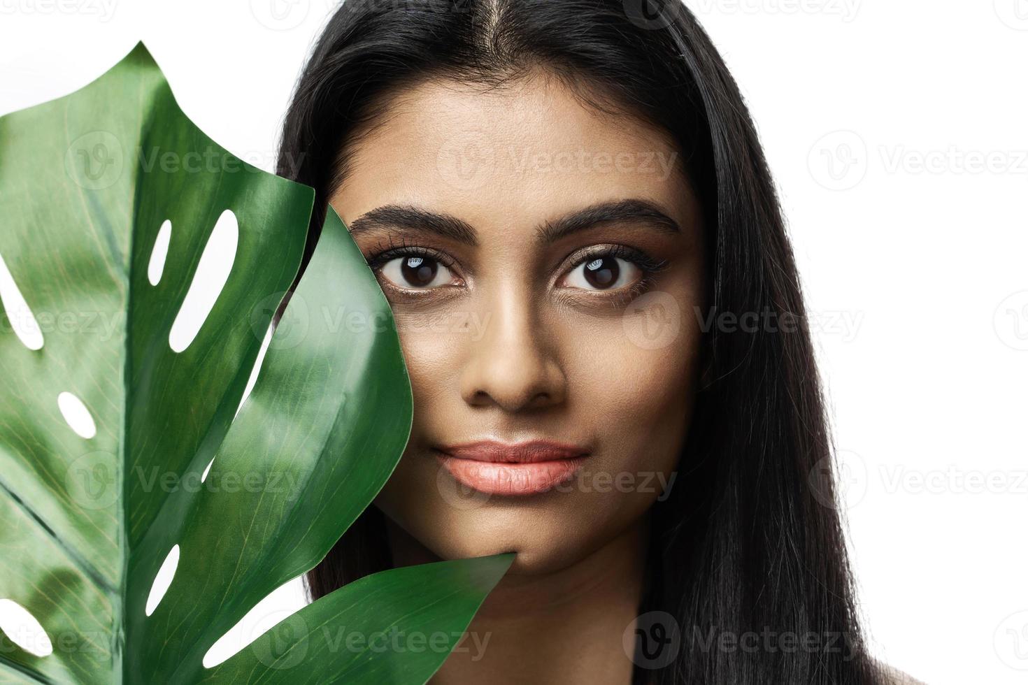 schöne indische frau mit einer glatten haut, die grünes tropisches blatt hält foto