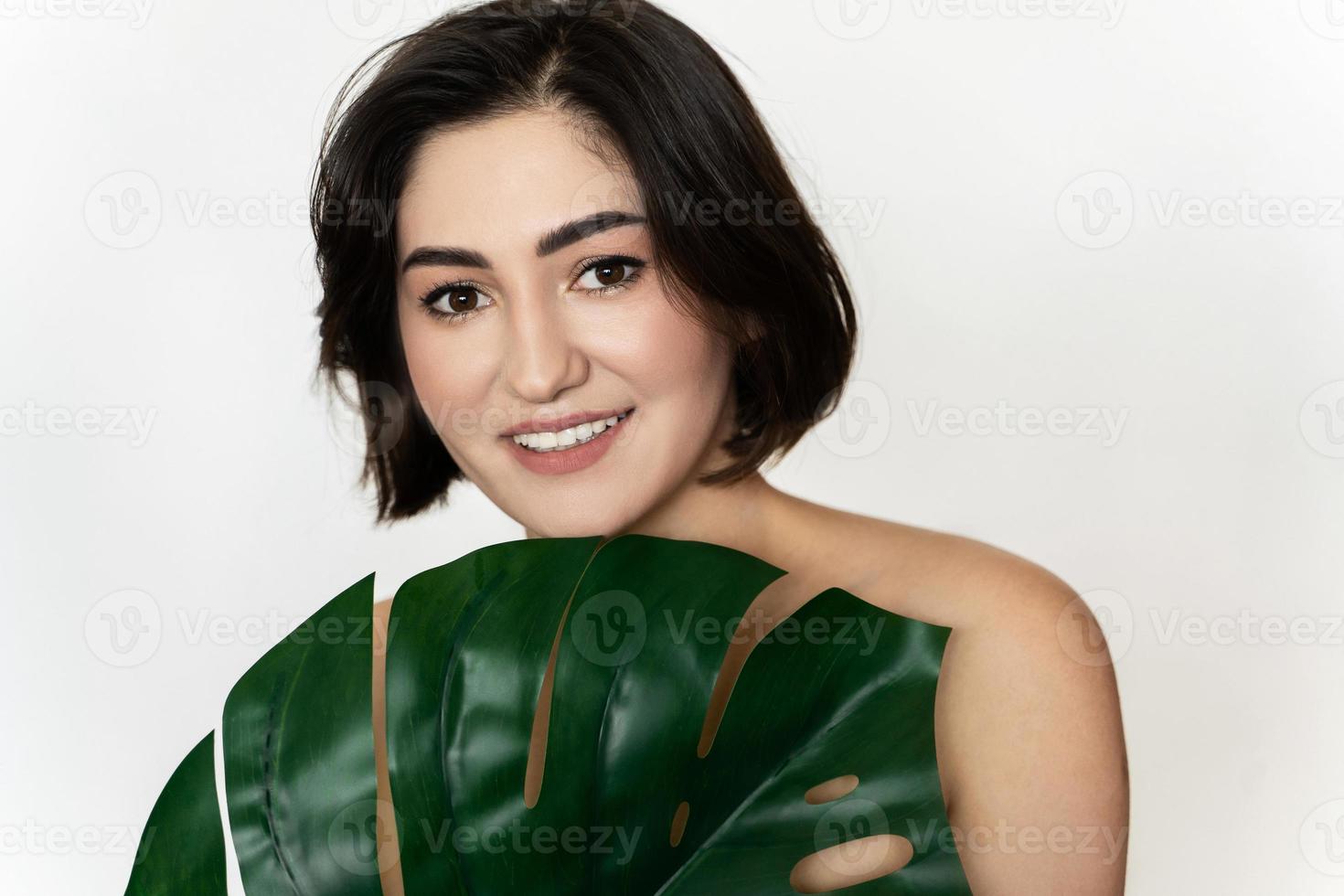 Porträt einer jungen, schönen, brünetten Frau mit einem tropischen Blatt von Monstera Deliciosa foto