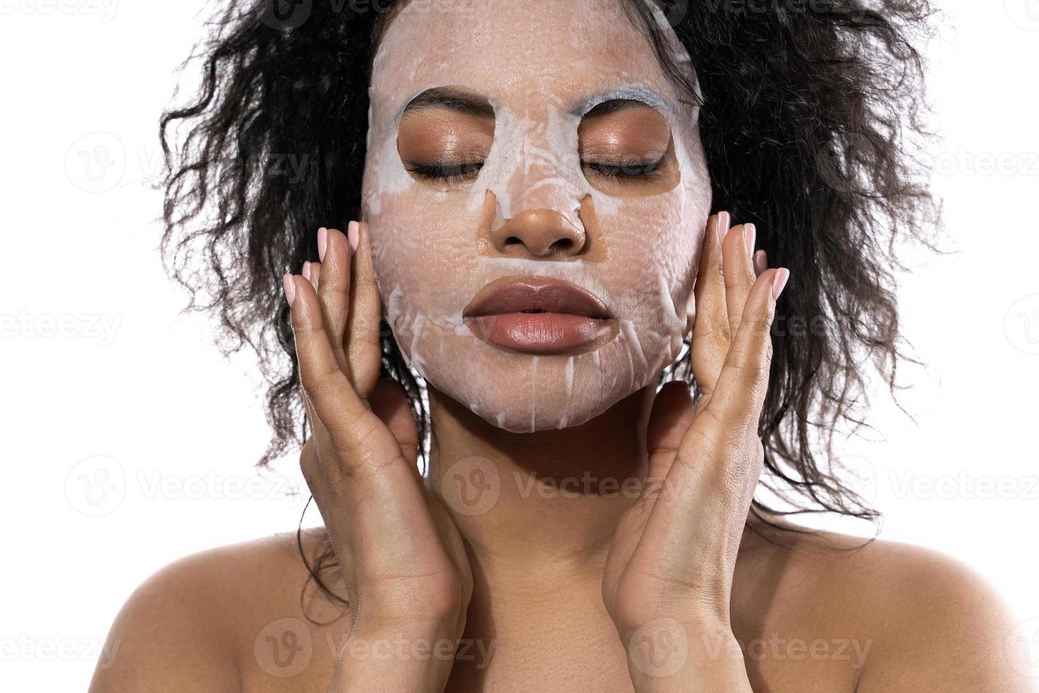 schöne schwarze frau mit einer glatten haut, die gesichtsblattmaske anwendet foto