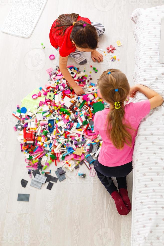 Kinder spielen mit einem Spielzeugdesigner auf dem Boden des Kinderzimmers. Zwei Kinder spielen mit bunten Blöcken. Kindergarten Lernspiele. foto
