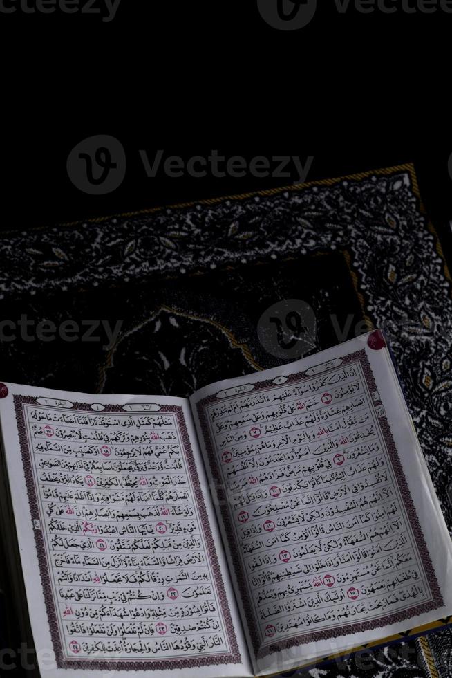 al-Quran, der sich über dem Gebetsteppich mit schwarzem Hintergrund befindet foto