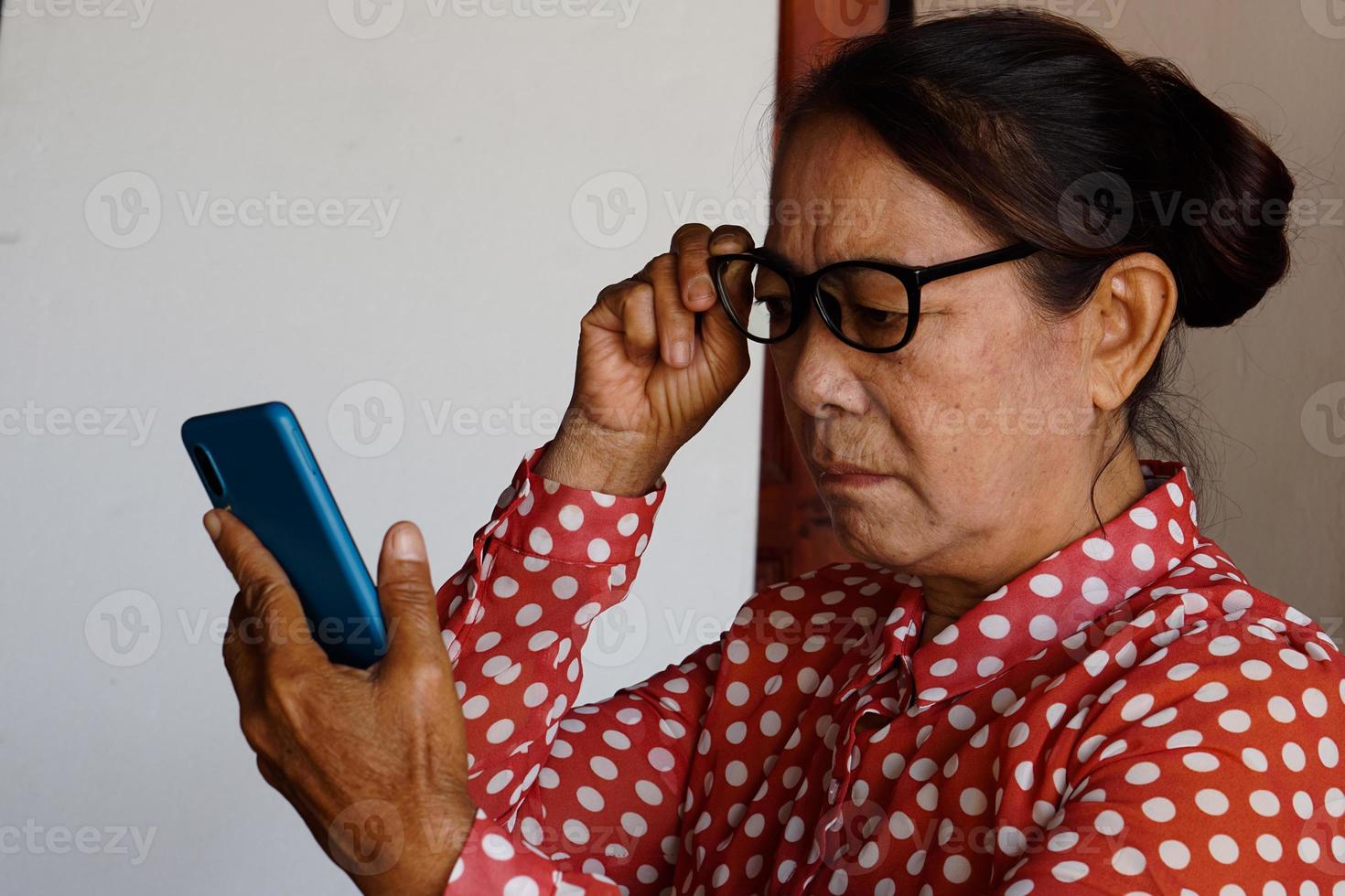 asiatische Seniorin hat Probleme mit dem Sehvermögen beim Betrachten des Smartphones, hält eine Brille. Konzept, Heideproblem foto