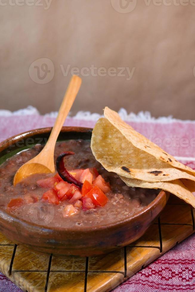 bohnen gekocht in einem lehmgericht mit tomaten und tortillas, mexikanisches armes gericht foto