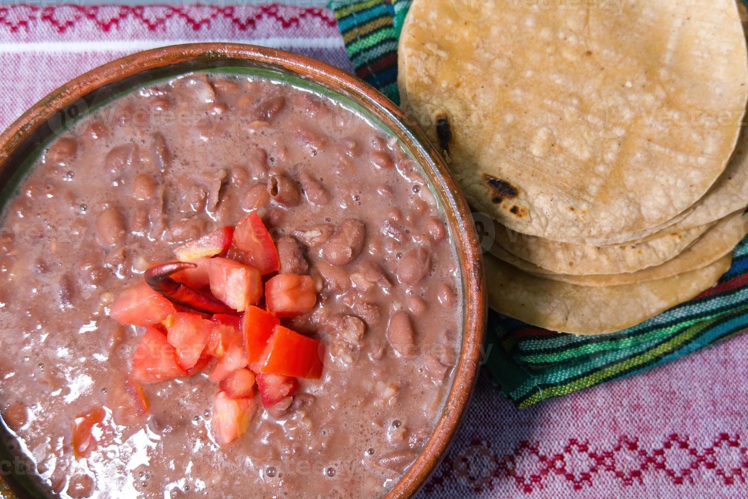 bohnen gekocht in einem lehmgericht mit tomaten und tortillas, mexikanisches armes gericht foto