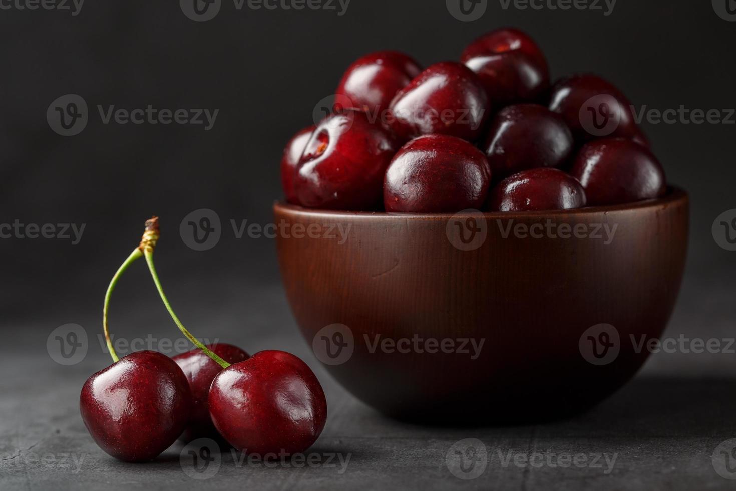 Reife und saftige Kirschbeeren auf einem schwarzen strukturierten Hintergrund in einer braunen Tasse mit Wassertropfen. Draufsicht, Nahaufnahme. foto