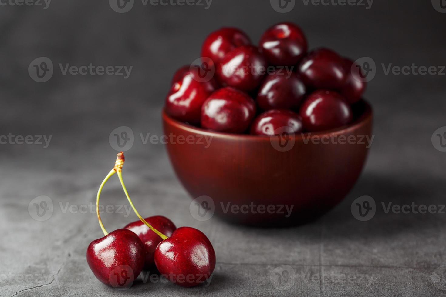 Reife und saftige Kirschbeeren auf einem schwarzen strukturellen Hintergrund in einer braunen Tasse mit Wassertropfen. Draufsicht, Nahaufnahme, Makro. foto