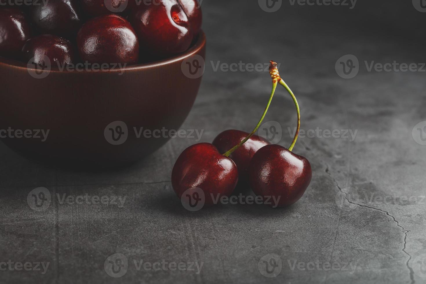 Reife und saftige Kirschbeeren auf einem schwarzen strukturellen Hintergrund in einer braunen Tasse mit Wassertropfen. Draufsicht, Nahaufnahme, Makro. foto