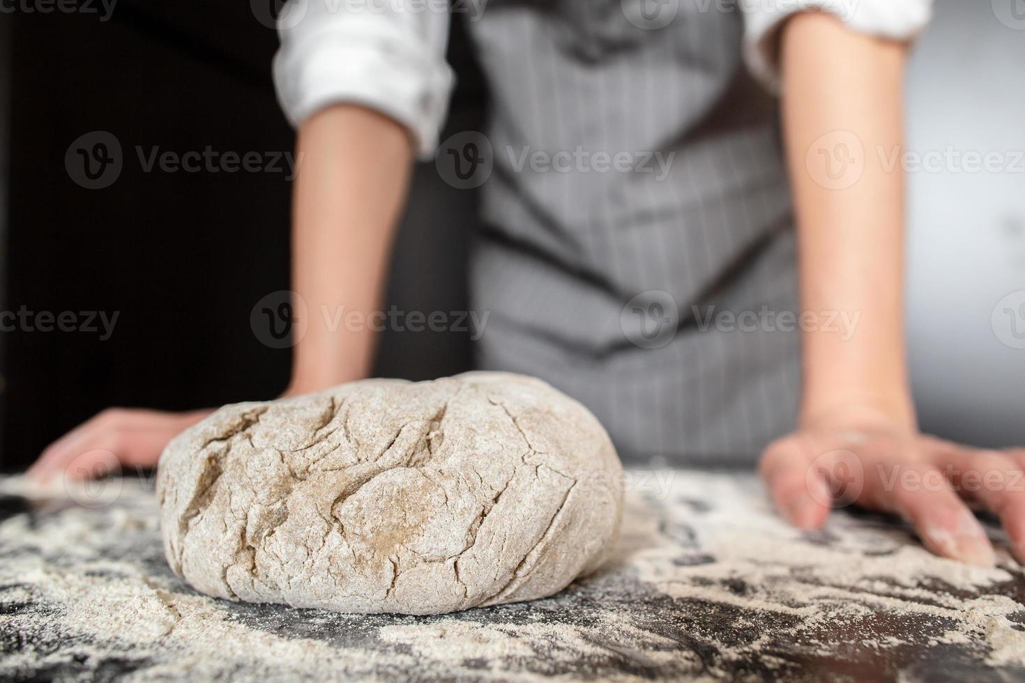 Der vorbereitete Teig liegt auf dem mit Mehl bestreuten Tisch vor dem Hintergrund der Bäckerhände. Brot machen. foto