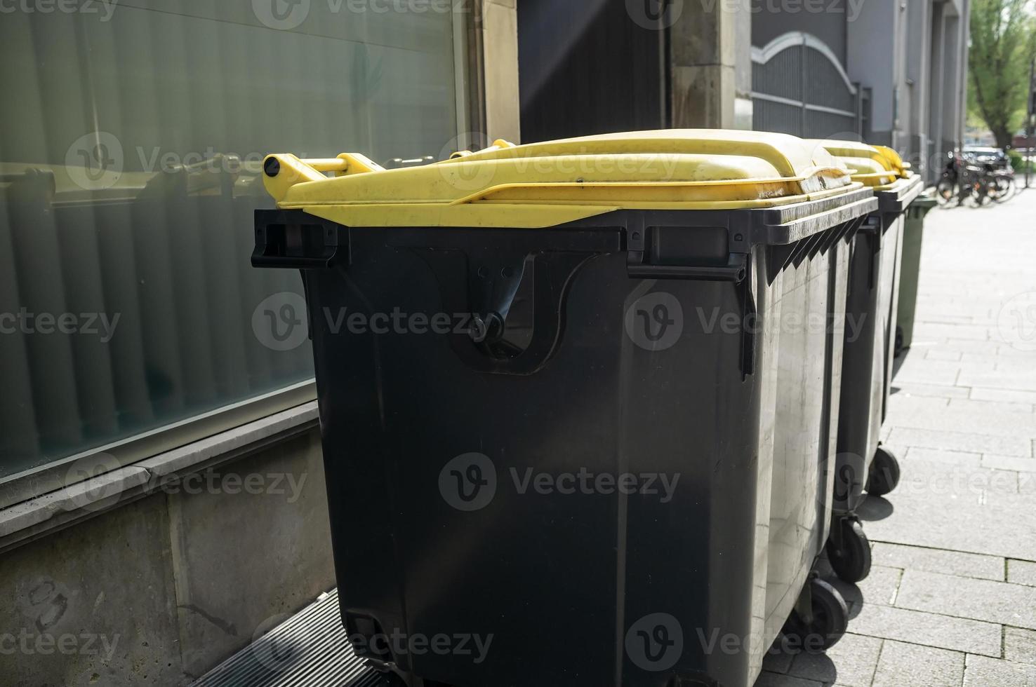 Müllcontainer aus Kunststoff stehen an einem Frühlingstag in der Nähe des Schaufensters des Gebäudes auf einer Stadtstraße. foto