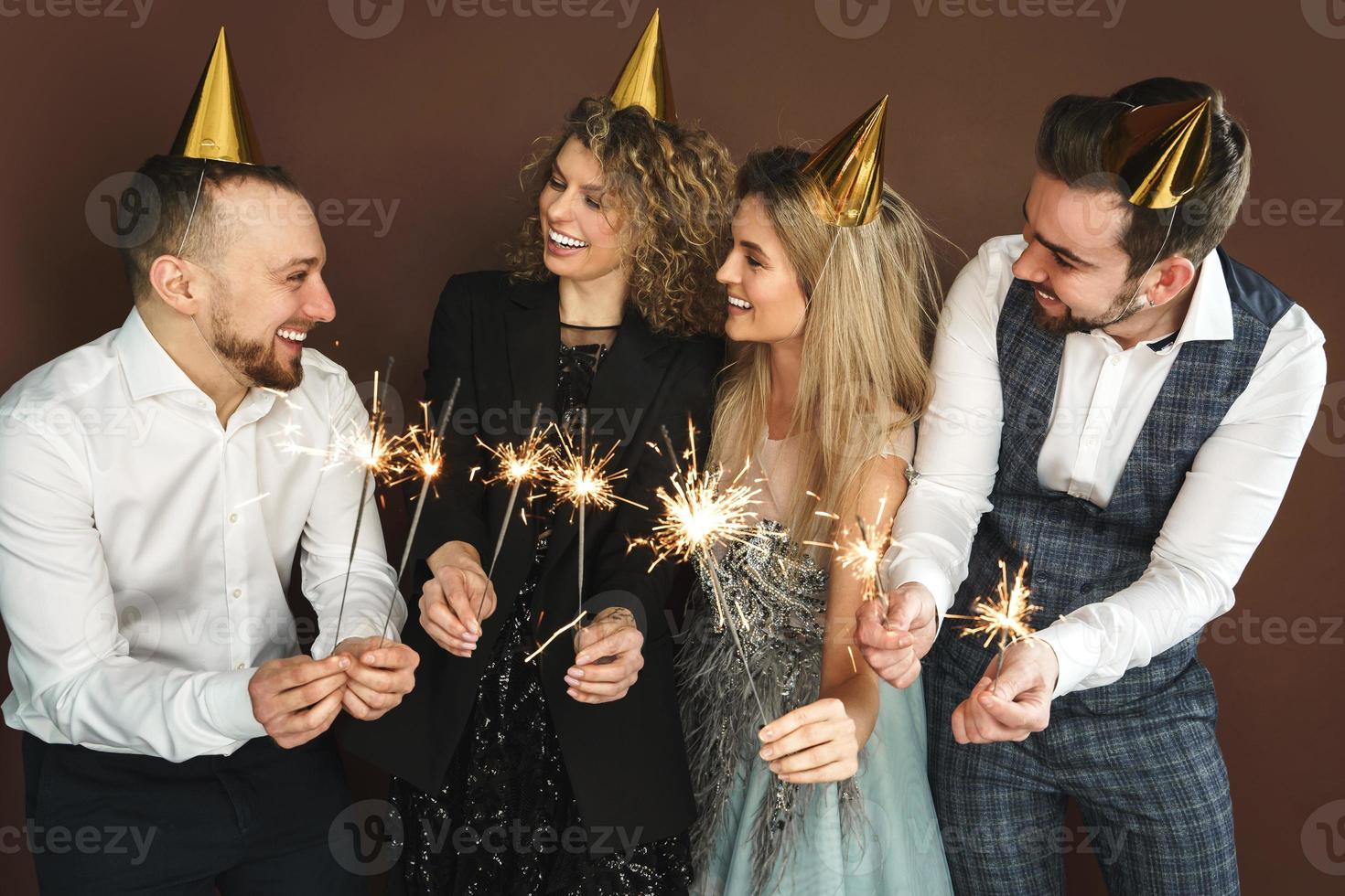 glückliche leute, die partyhüte tragen, die brennende funkeln während der feiertags- oder veranstaltungsfeier halten foto