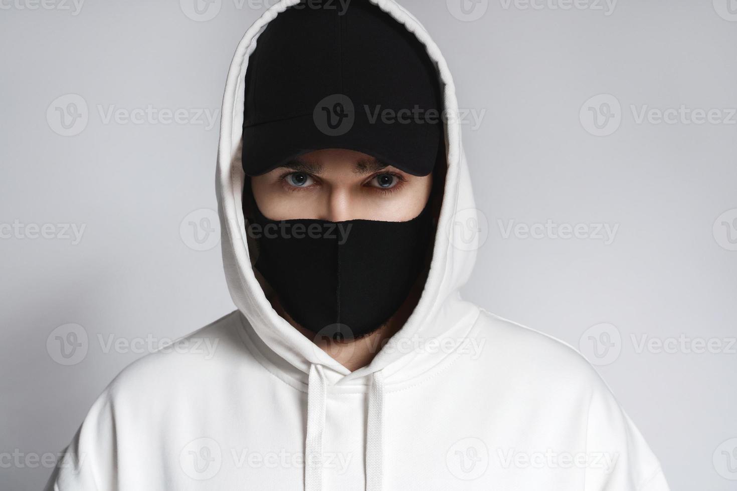 Mann mit weißem Kapuzenpullover, schwarzer Baseballkappe und Stoffgesichtsmaske foto