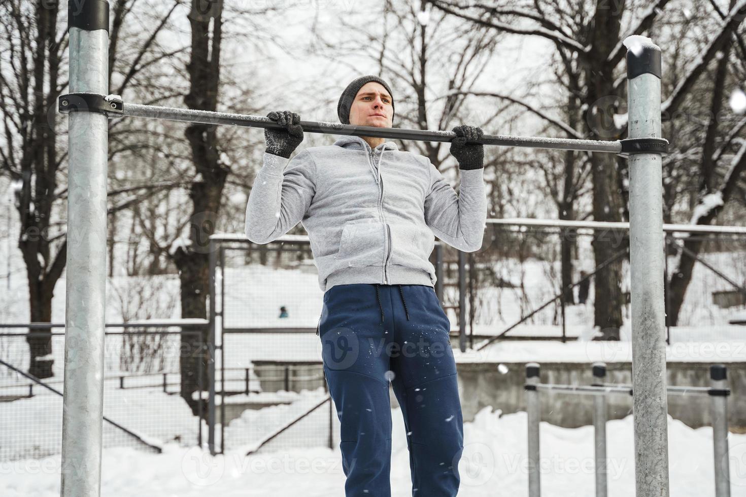 sportlicher Mann, der während seines Wintertrainings im Freien Klimmzüge an der horizontalen Stange macht foto