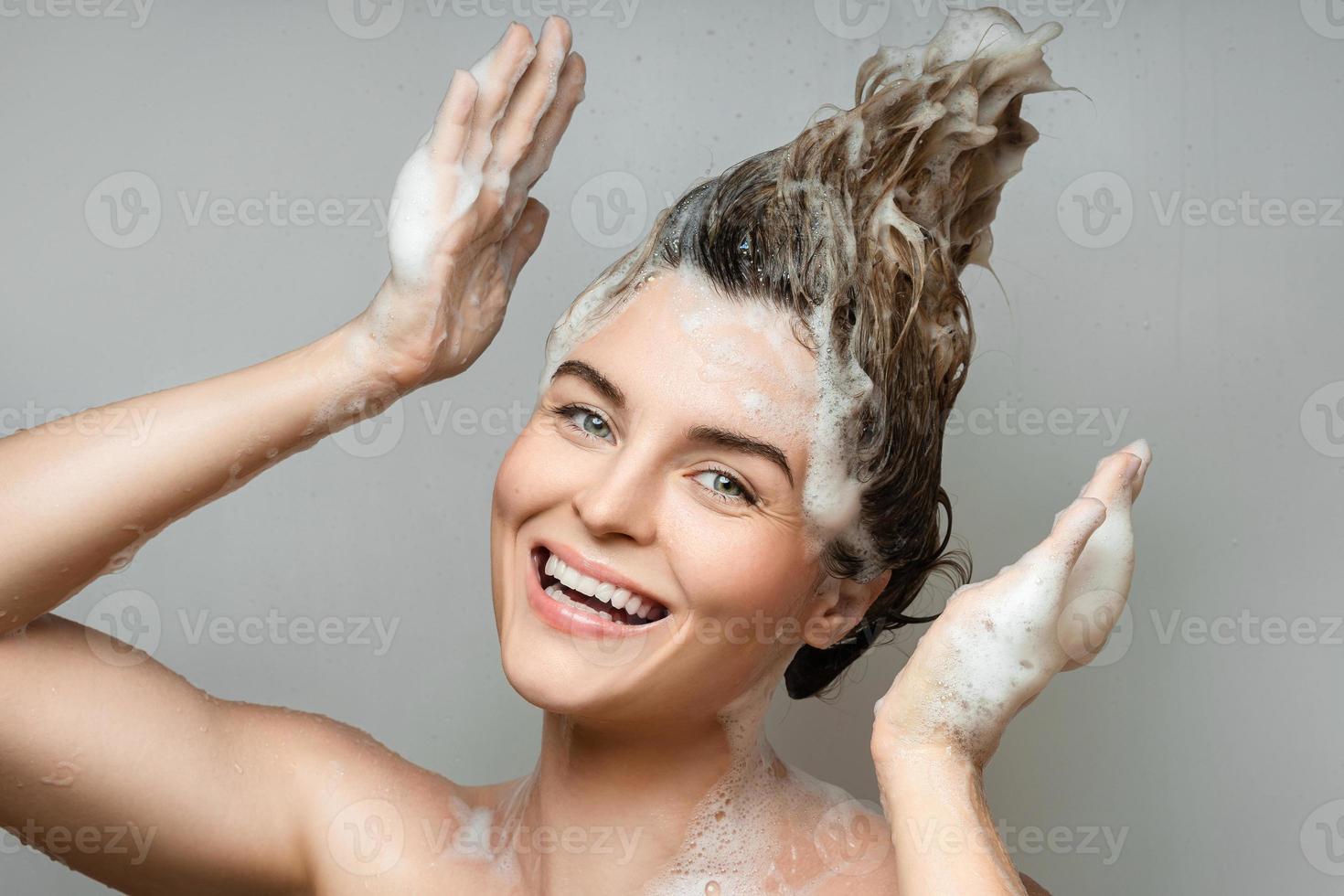 Fröhliche schöne Frau wäscht sich die Haare mit einem Shampoo foto