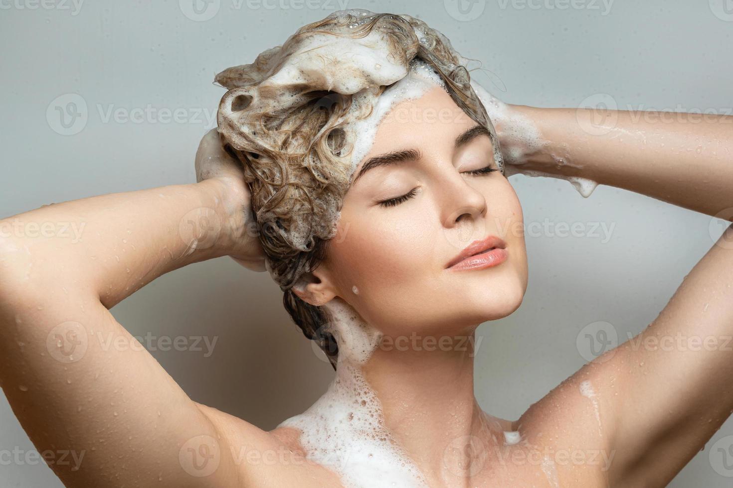 junge schöne frau wäscht sich die haare mit einem shampoo foto