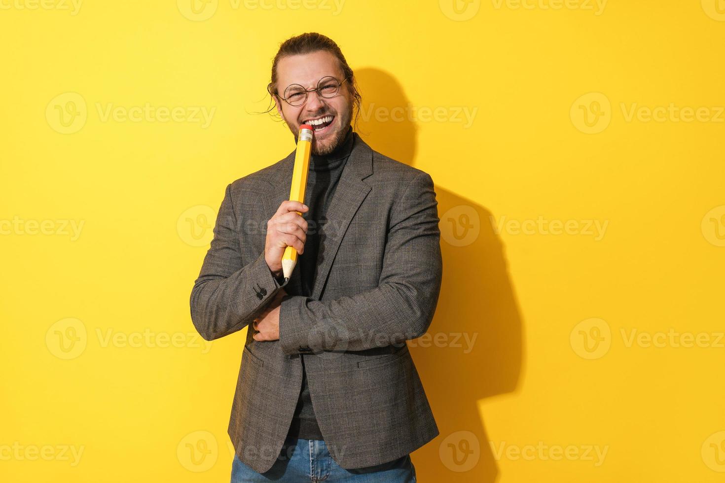 Fröhlicher Mann mit Brille, der große Stifte auf gelbem Hintergrund hält foto