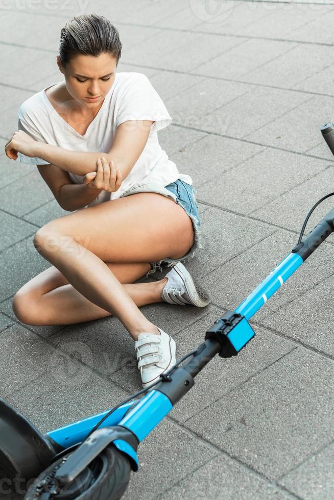 junge Frau, die nach einem Unfall mit einem E-Scooter unter Ellbogenschmerzen leidet foto