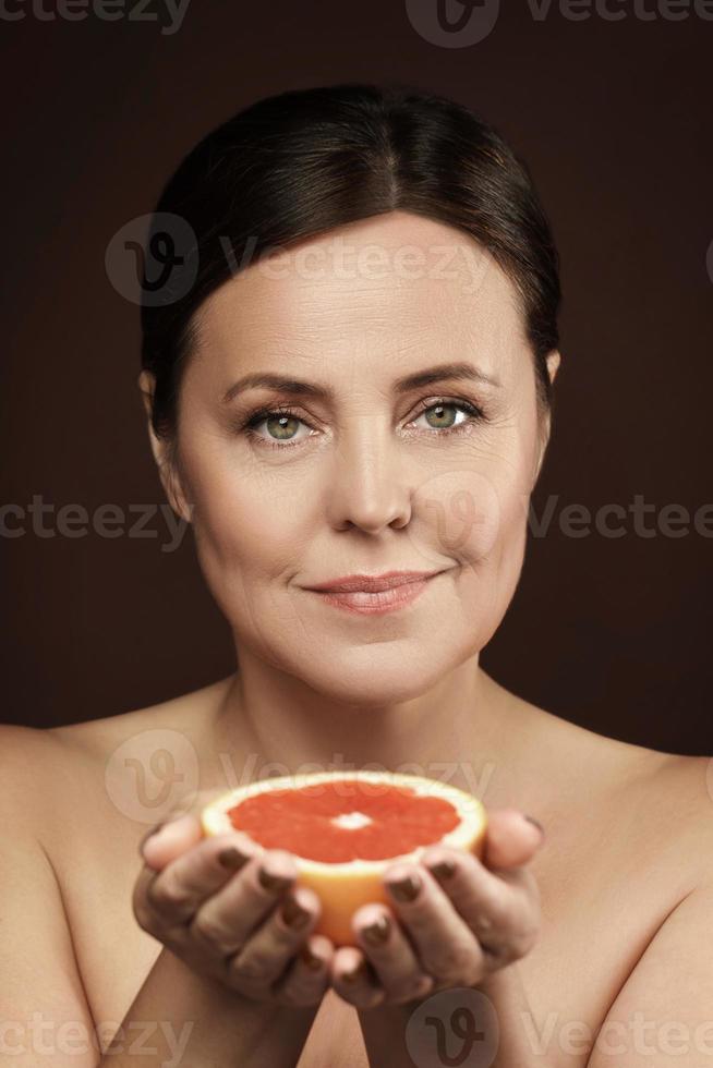 schöne und glückliche Frau mittleren Alters mit einer Grapefruit in der Hand foto