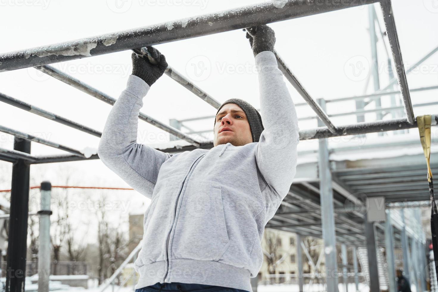 sportlicher Mann, der während seines Wintertrainings im Freien Klimmzüge an der horizontalen Stange macht foto