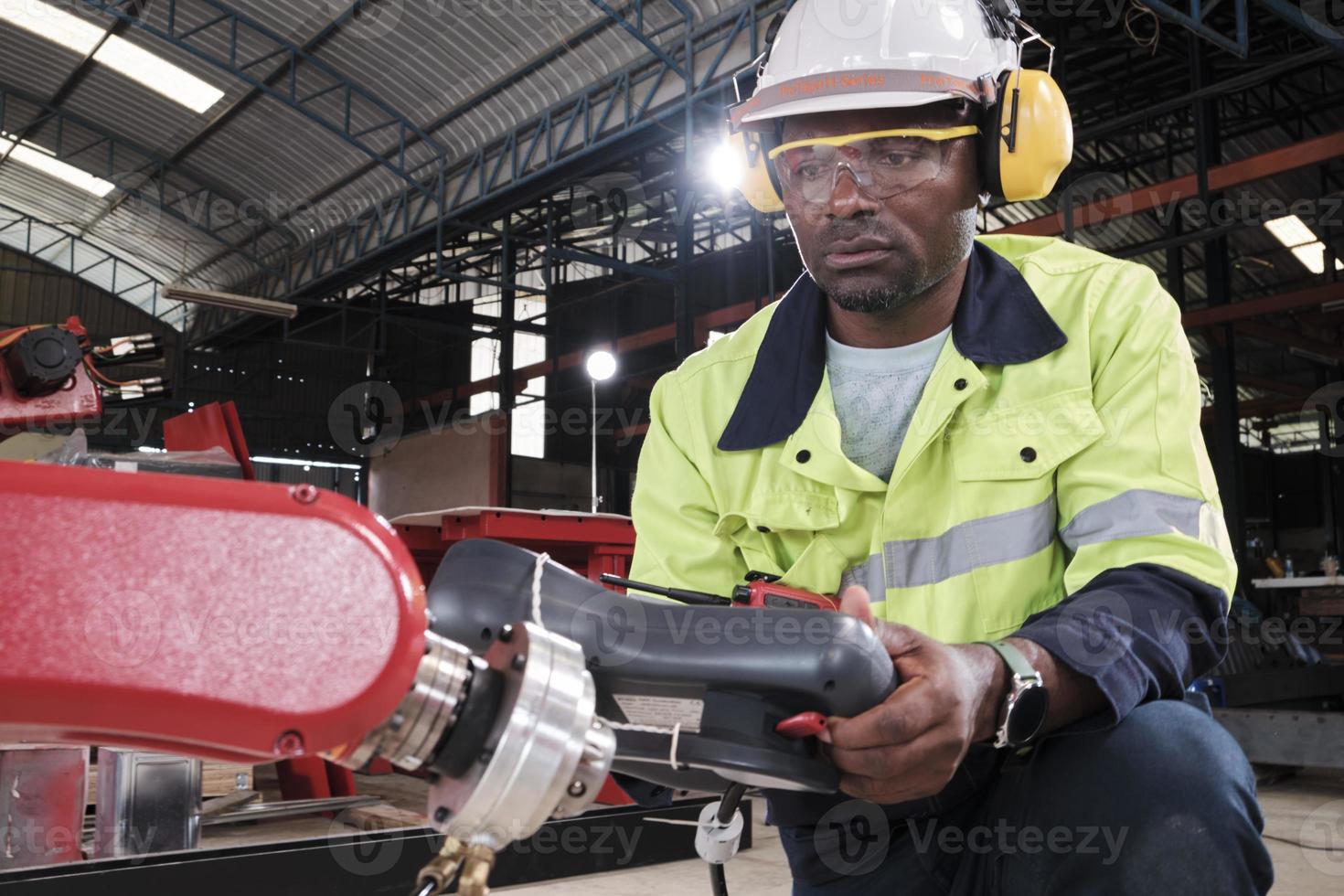 Ein afroamerikanischer Produktionsingenieur testet und steuert Roboterarme in einer mechanischen Fertigungsfabrik, intelligente automatische Maschinen im Industriegeschäft und futuristische Technologieinnovationen. foto