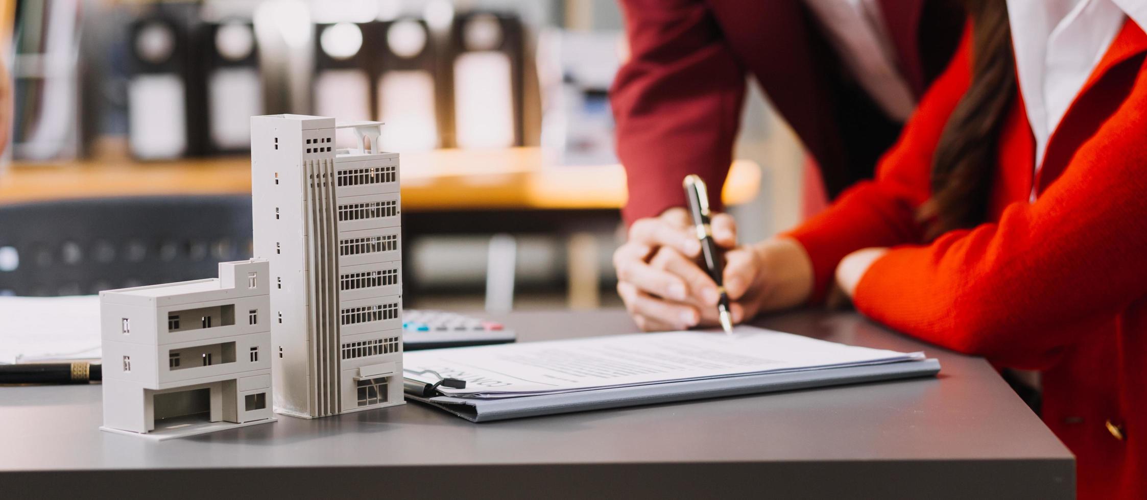 Diskussion mit einem Immobilienmakler, Hausmodell mit Makler und Kunde, der für den Kaufvertrag, den Abschluss einer Versicherung oder das Darlehen von Immobilien oder Grundstücken bespricht. foto