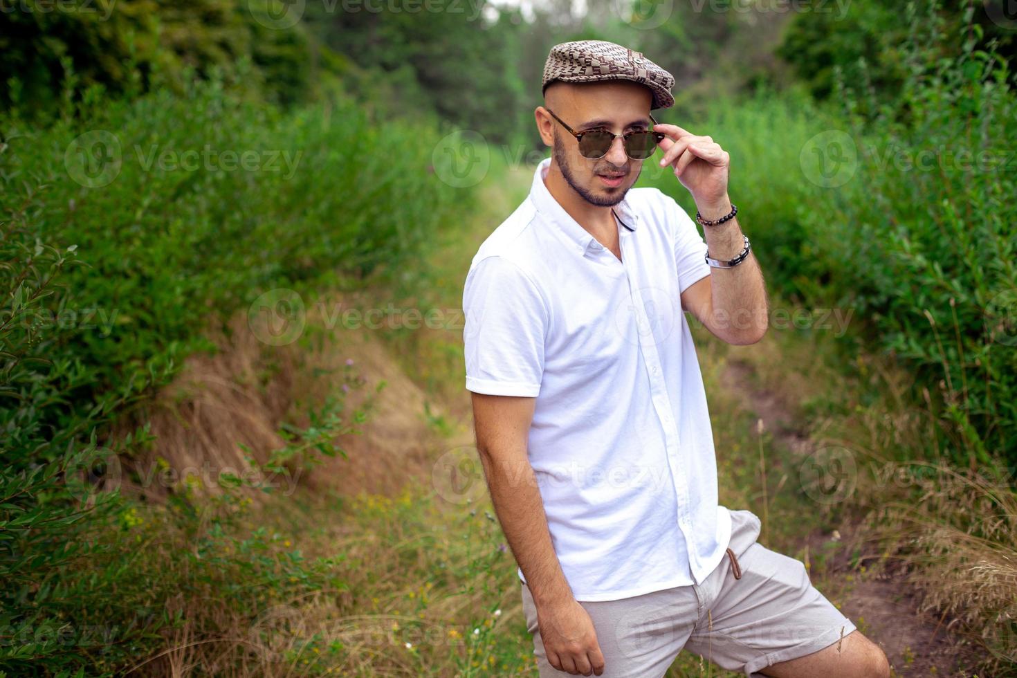 Porträt eines wunderschönen jungen Mannes mit Hut und Sonnenbrille, der auf den grünen Park blickt foto