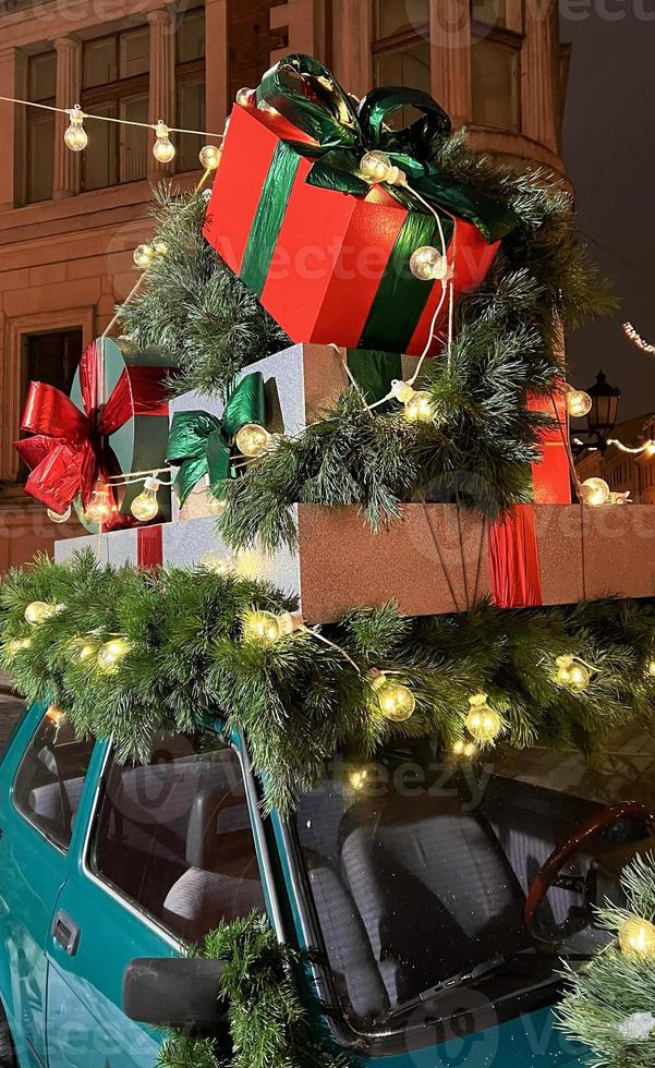 Santas alter Oldtimer mit Geschenkboxen an der Spitze. nahaufnahmezweige von nadelbäumen, die mit einer glänzenden lichtgirlande verziert sind. perfekter festlicher inhalt für geschichtenhintergrund, vertikales banner. foto