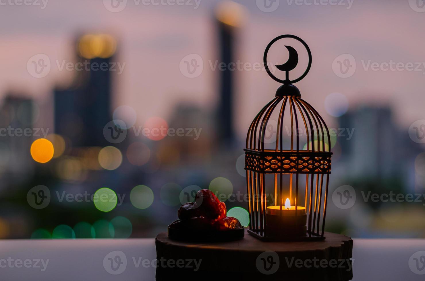 laterne mit mondsymbol oben und dattelfrüchten auf holztablett mit bunten stadt-bokeh-lichtern für das muslimische fest des heiligen monats ramadan kareem. foto