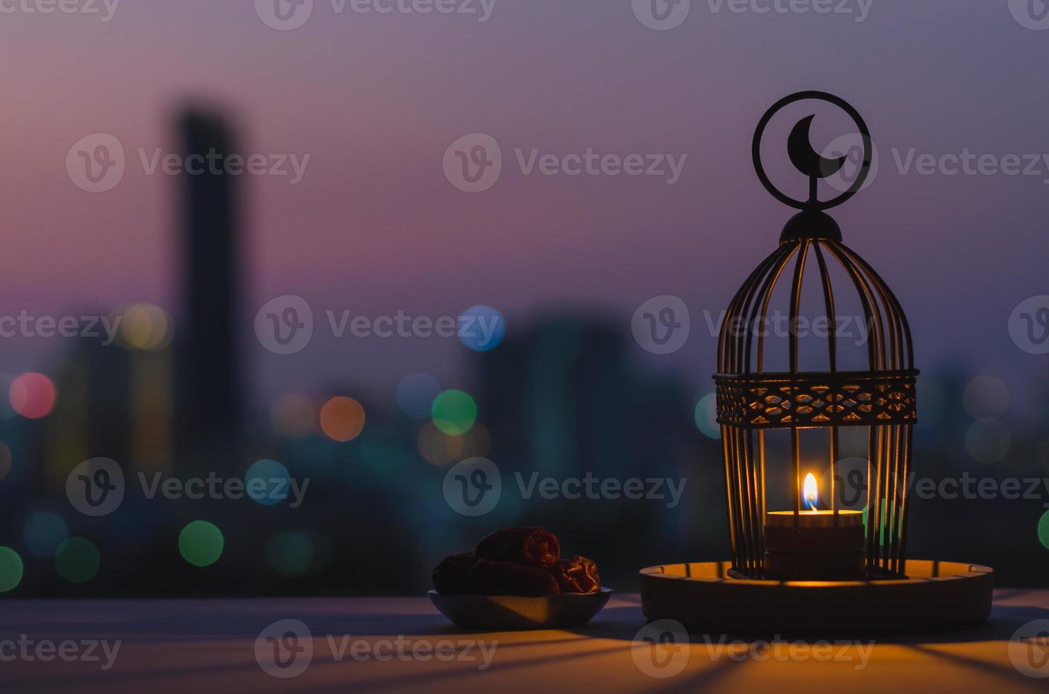 laterne mit mondsymbol oben und kleinem teller mit dattelfrüchten mit abendhimmel und stadt-bokeh-lichthintergrund für das muslimische fest des heiligen monats ramadan kareem. foto