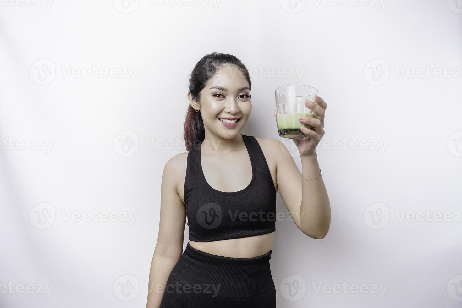 Fröhliche, sportliche asiatische Frau, die Sportkleidung mit einem Glas leckeren grünen Smoothie trägt, isoliert auf weißem Hintergrund. foto