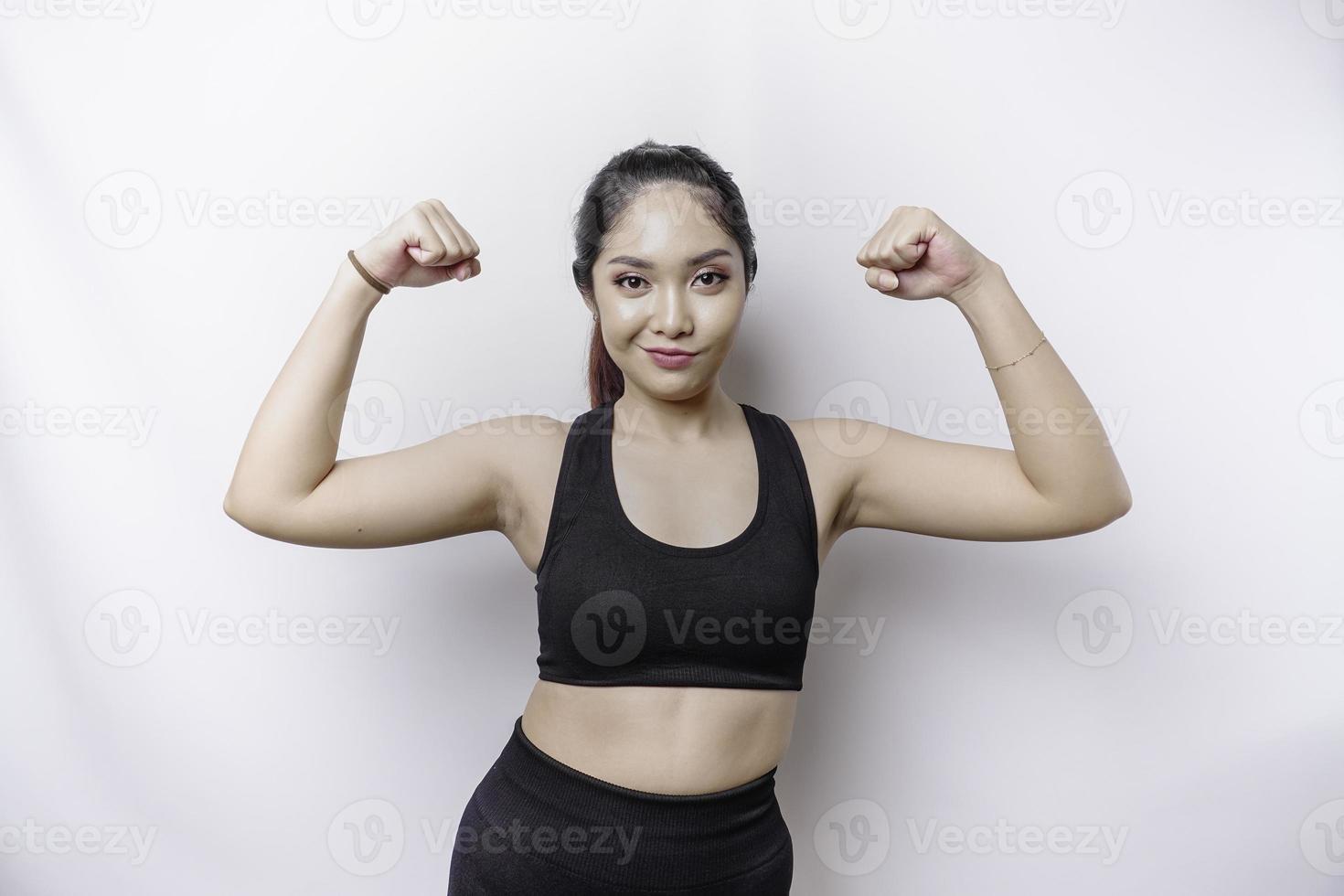 Aufgeregte asiatische sportliche Frau, die eine Sportkleidung trägt, die eine starke Geste zeigt, indem sie stolz ihre Arme und Muskeln hebt und lächelt foto