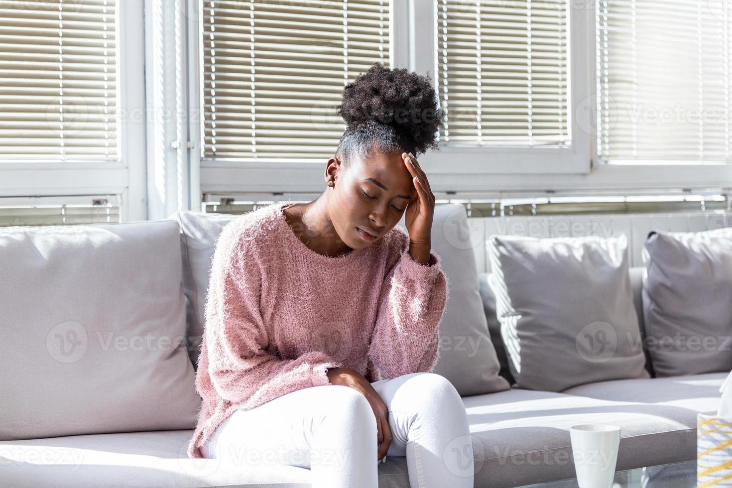 Porträt eines jungen schwarzen Mädchens, das zu Hause mit Kopfschmerzen und Rückenschmerzen auf der Couch sitzt. schöne frau, die unter chronischen täglichen kopfschmerzen leidet. traurige frau, die ihren kopf hält, weil nebenhöhlenschmerzen foto