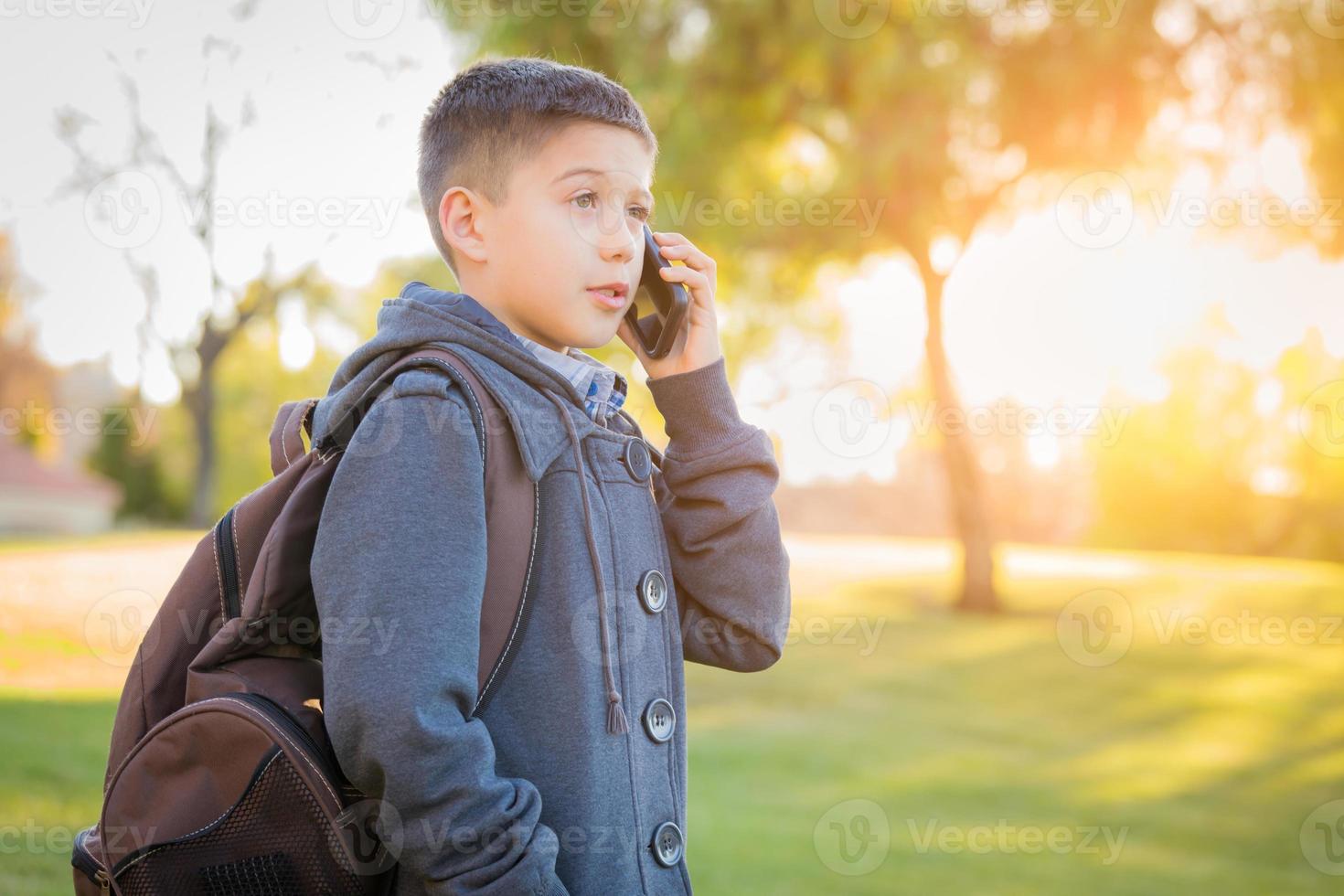 junger hispanischer Junge, der im Freien mit Rucksack spazieren geht und mit dem Handy spricht foto