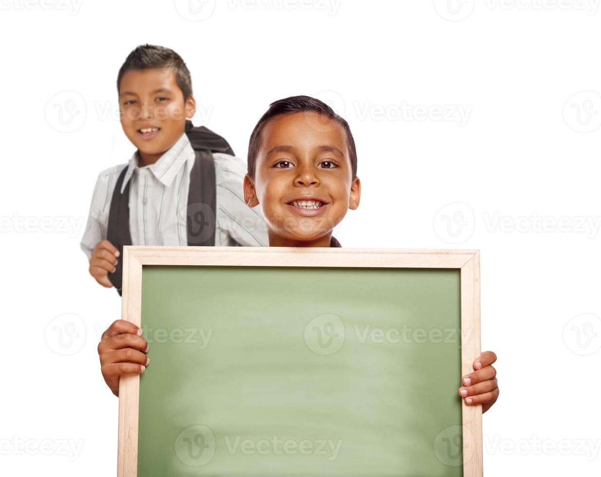 hispanische Jungen, die leere Kreidetafel auf weißem Hintergrund halten foto