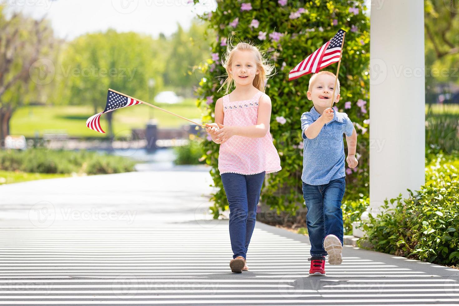 junge schwester und bruder schwenken amerikanische flaggen im park foto