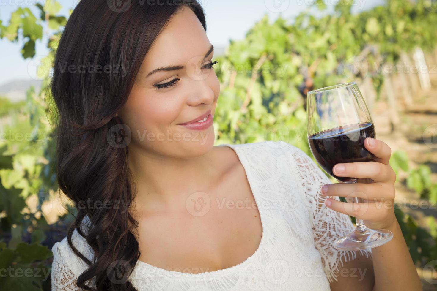 junge erwachsene frau, die ein glas wein im weinberg genießt foto