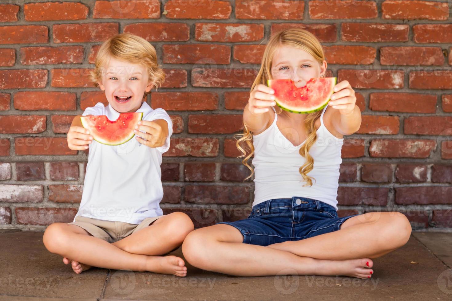 süßer junger cuacasischer junge und mädchen, die wassermelone gegen die mauer essen foto