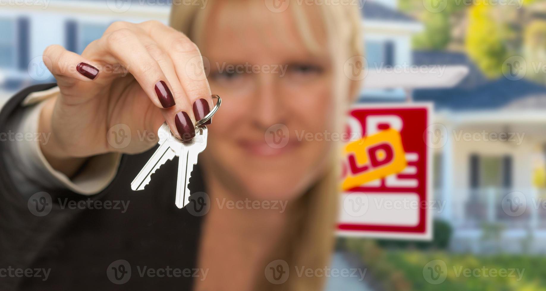 immobilienmakler überreicht neue hausschlüssel mit verkauftem schild dahinter foto